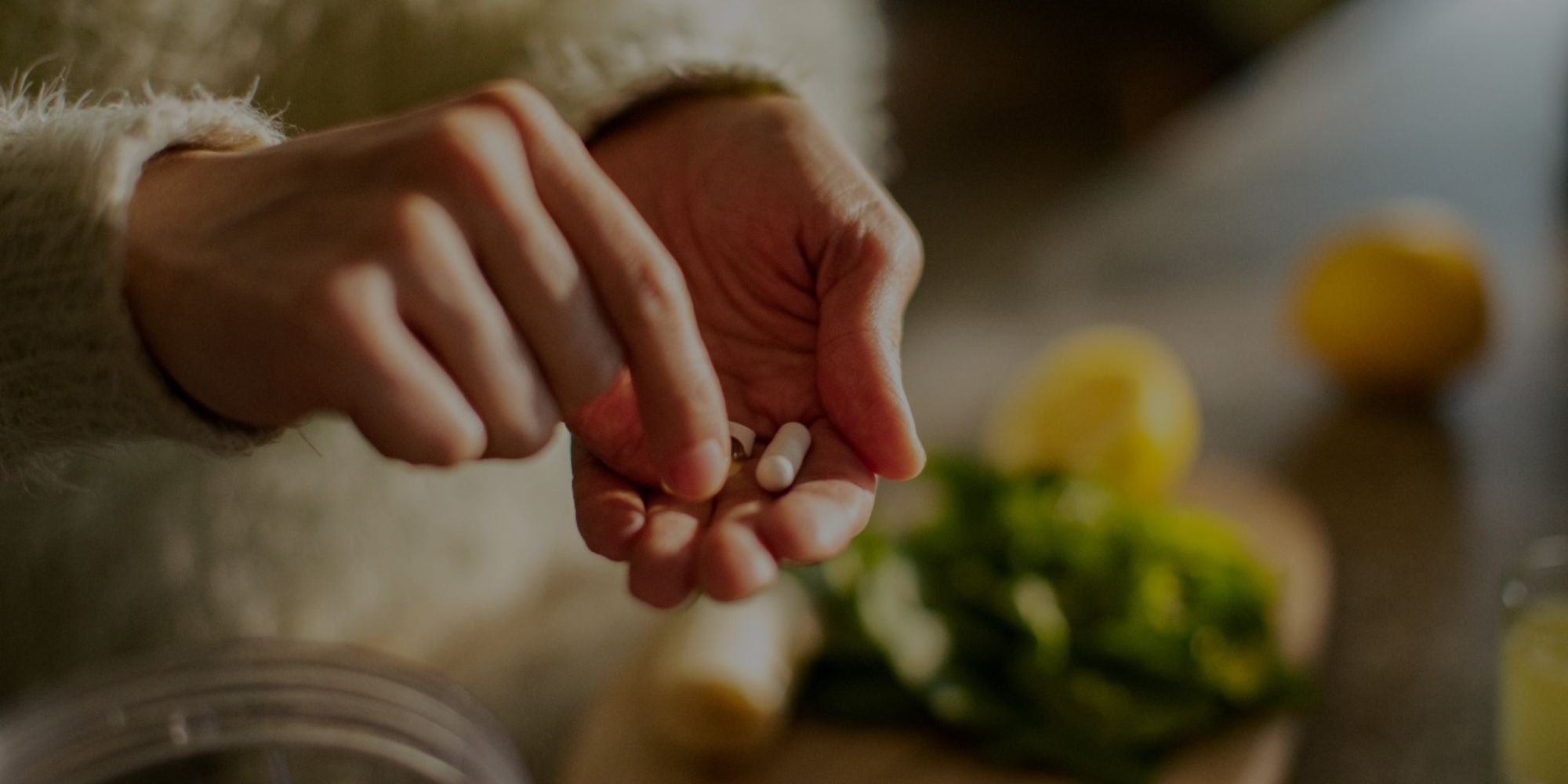 Woman's hands holding a small white supplement capsule near fresh vegetables